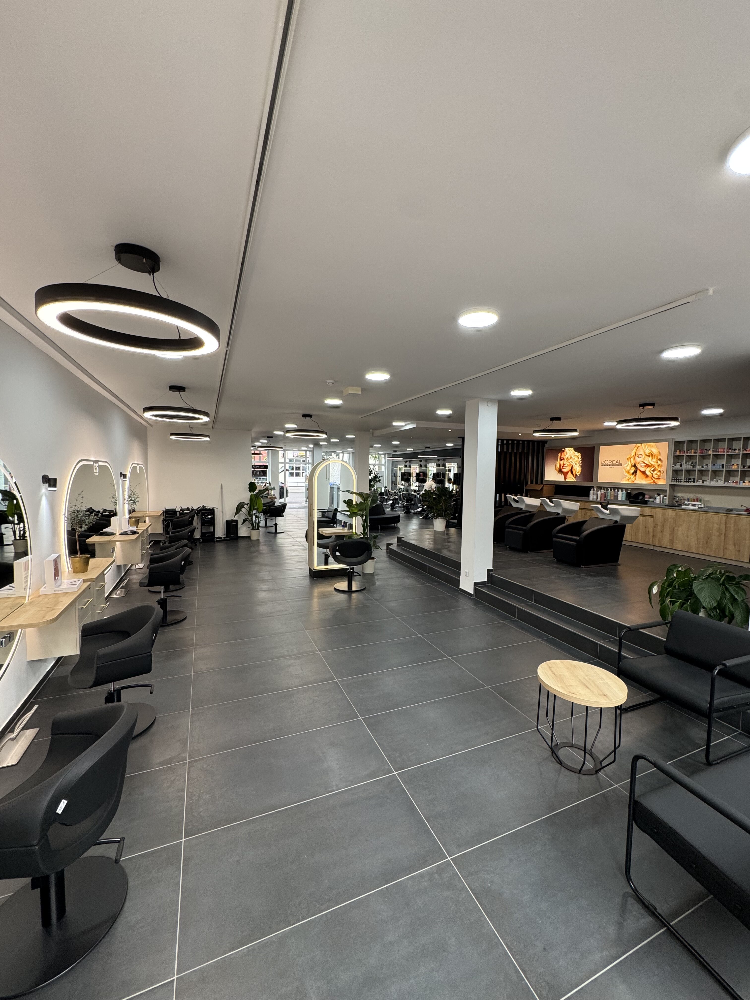 Moderner Friseursalon mit schwarzen Stühlen, hellem Boden und runden Spiegeln