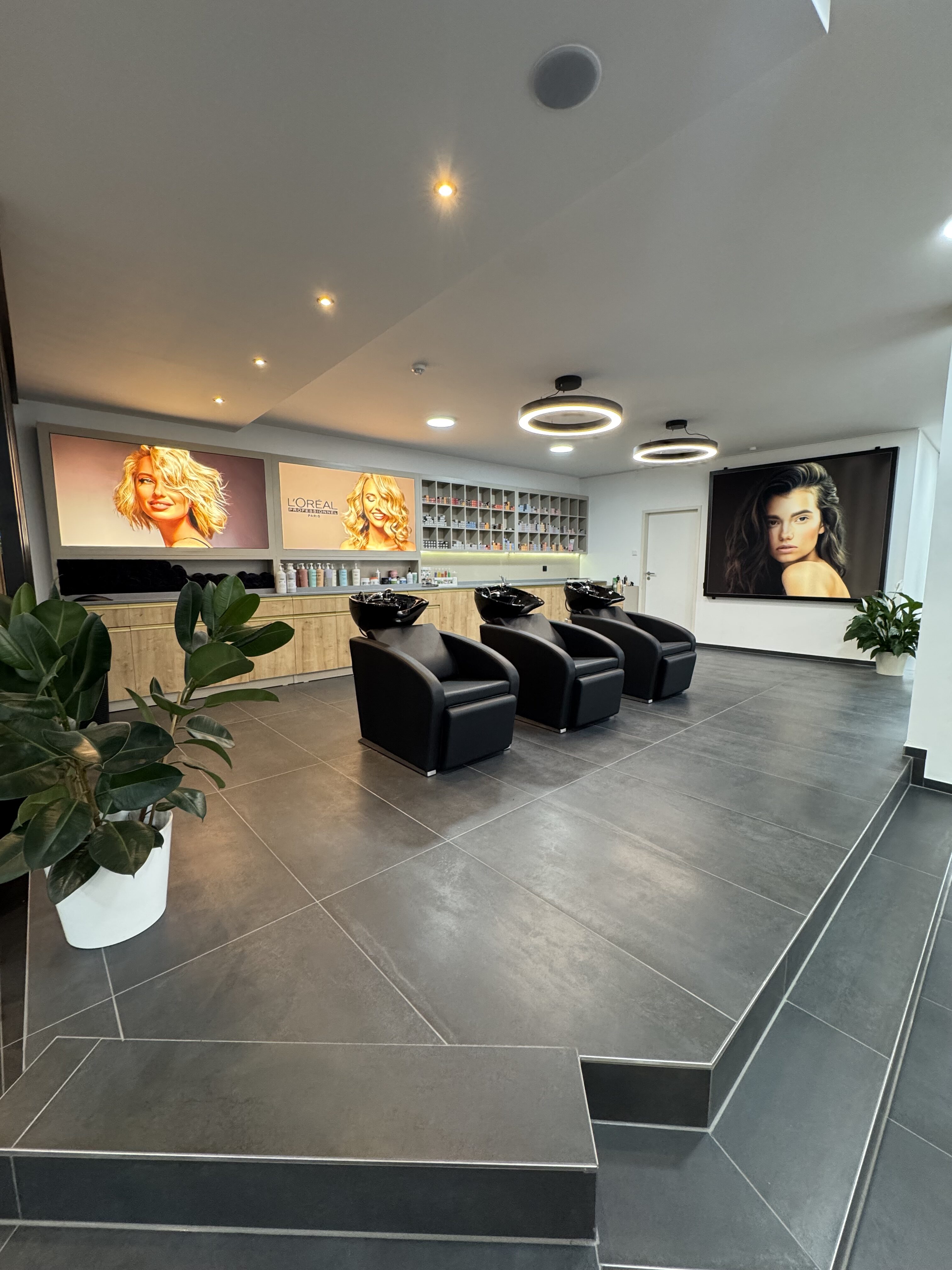 Moderner Friseursalon mit drei schwarzen Waschstühlen, Pflanzen und Werbepostern