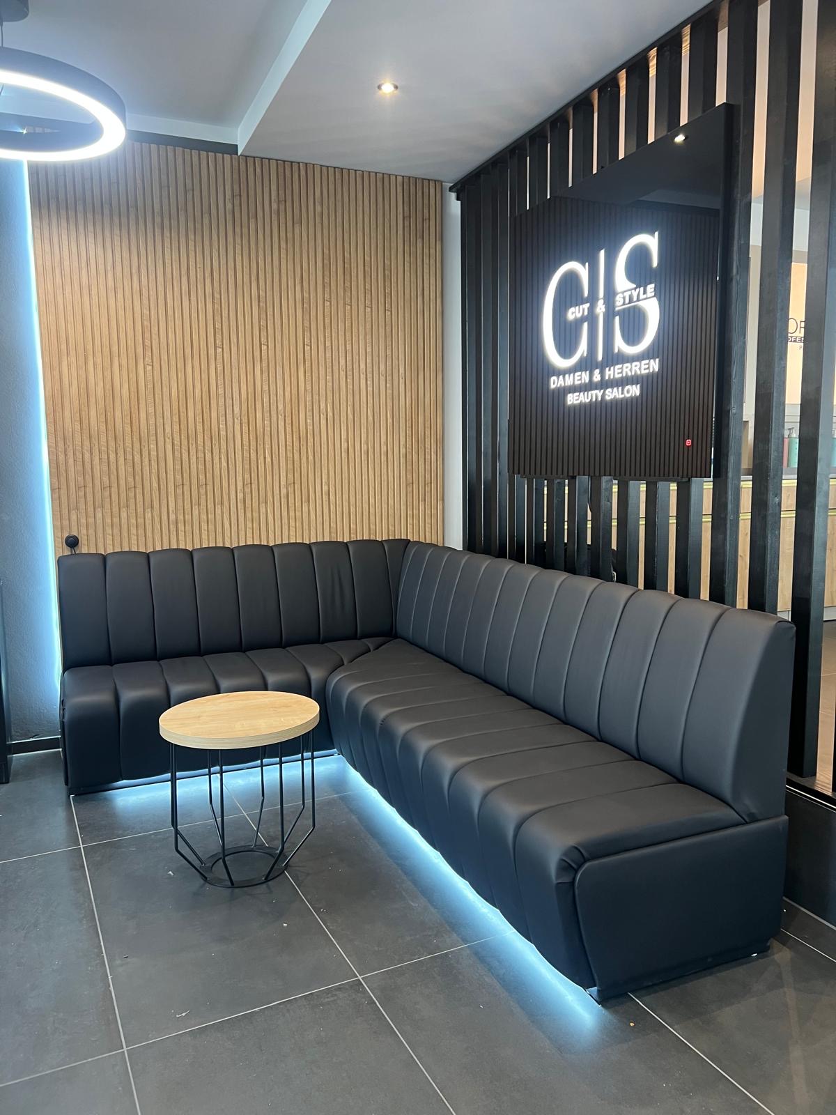 Eine schwarze Ledercouch in einer modernen Lounge mit Holzwand und leuchtendem Logo